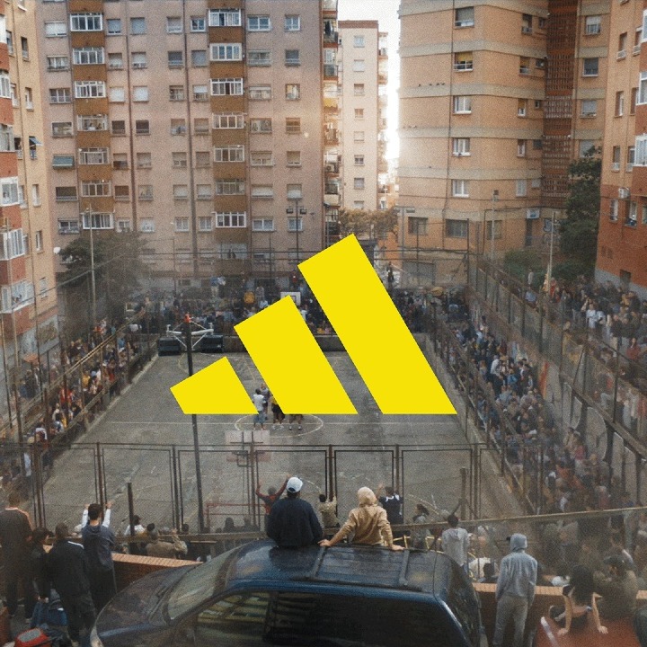 El logo de Adidas en amarillo sobre una cancha callejera rodeada de gente