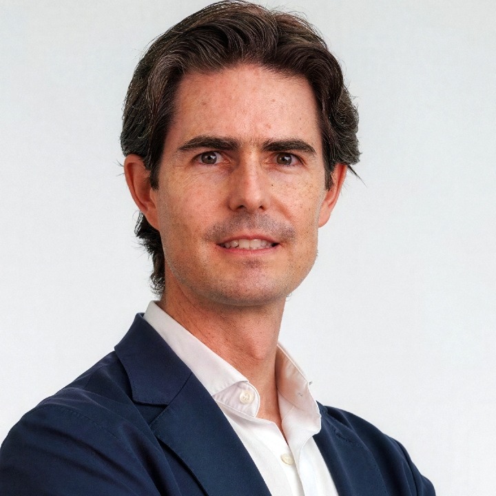 Un primer plano de Alejandro Guerra vestido con traje azul y camisa blanca