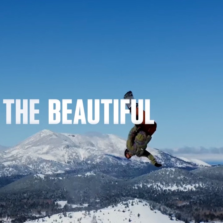Un hombre haciendo snowboard en la nieve con las letras sobreimpresas de "America the beautiful"