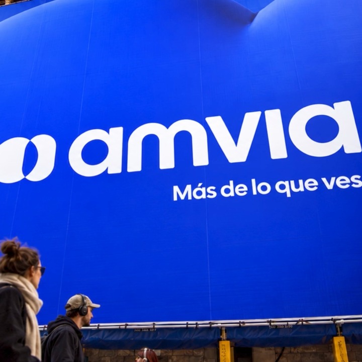 Personas caminando en la calle frente a una lona con el logotipo de Amvia