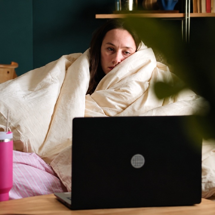Una mujer con cara triste enrollada en su edredón en el sofá viendo una serie
