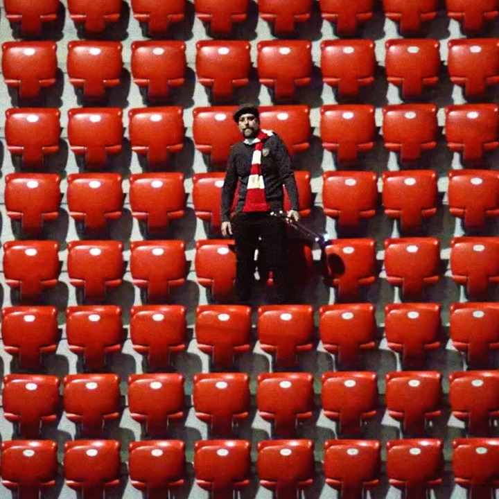 Un hombre en la grada rodeado de sillas rojas vacías