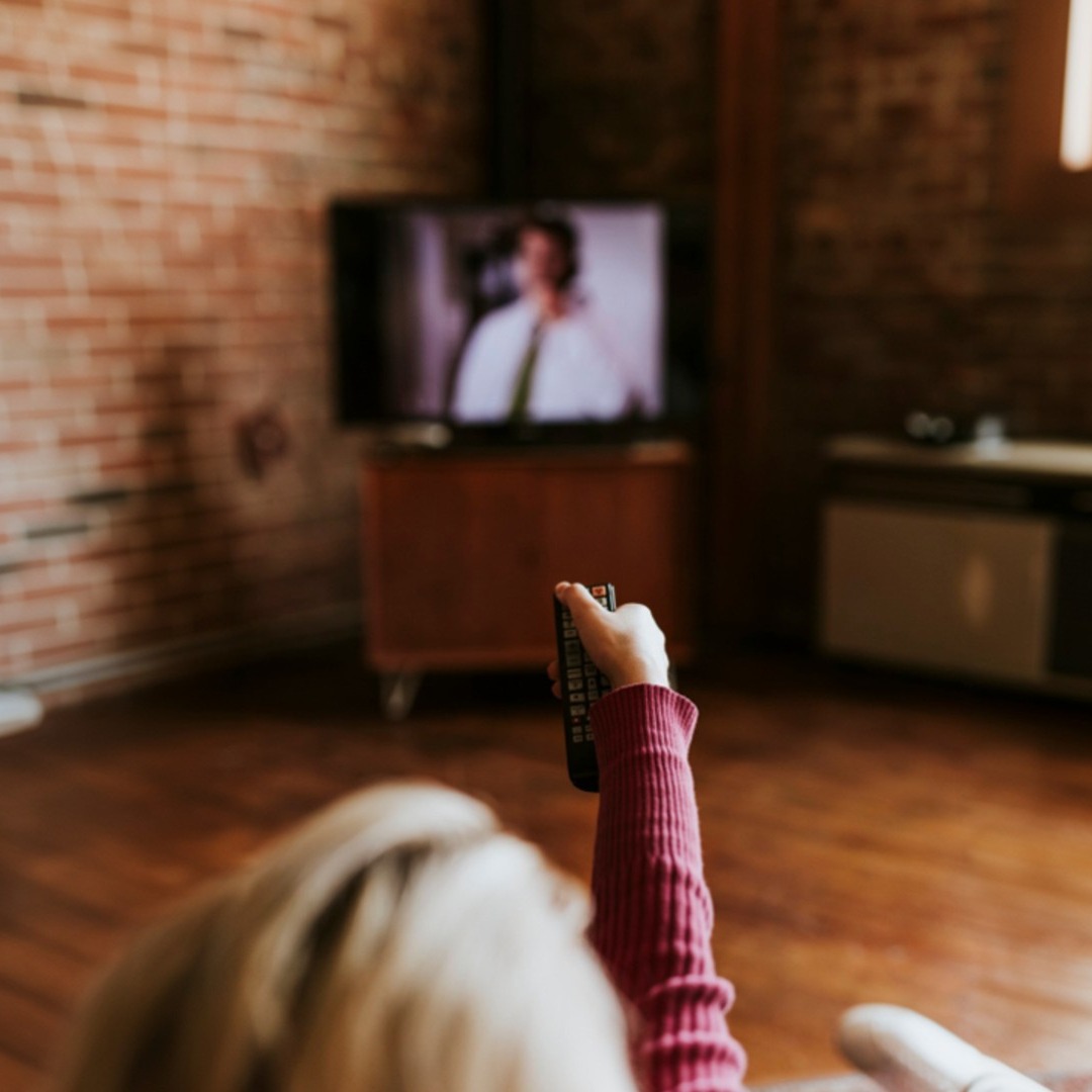 Una mujer sujeta un mando a distancia mientras ve la televisión