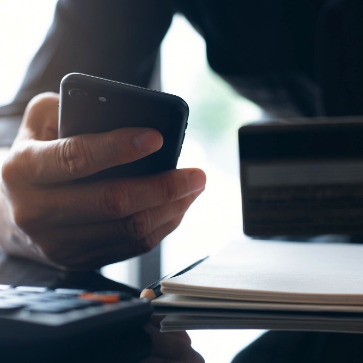 Una mano sostiene un móvil y la otra una tarjeta de crédito