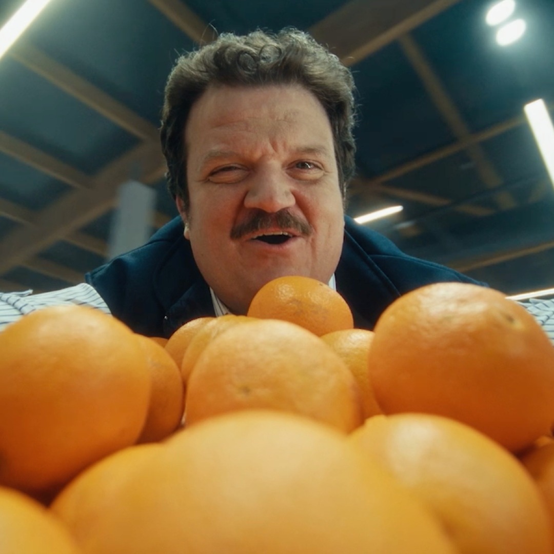 Un cajero canta apoyándose en la estantería de las naranjas de un supermercado