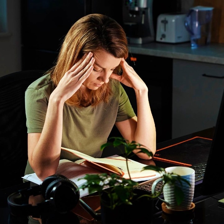 Una mujer que se lleva las manos a la cabeza en un gesto de agotamiento delante del ordenador en la cocina de su casa
