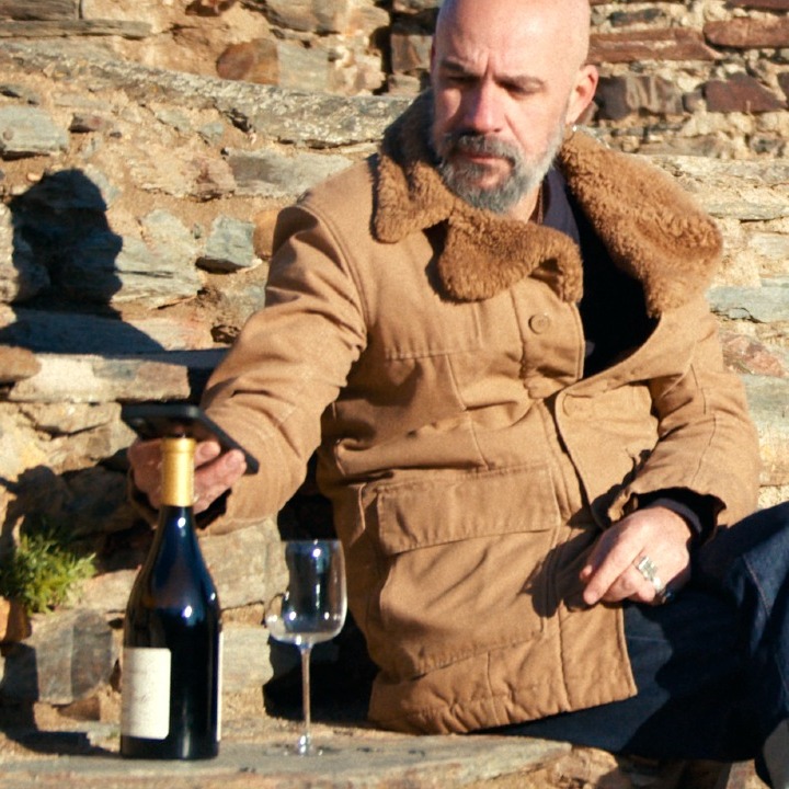 Un hombre sentado al sol acercando el móvil al corcho de una botella de vino