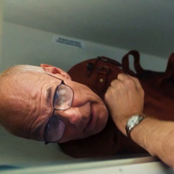 Una maleta con cabeza de señor que se está colocando en el maletero del avión