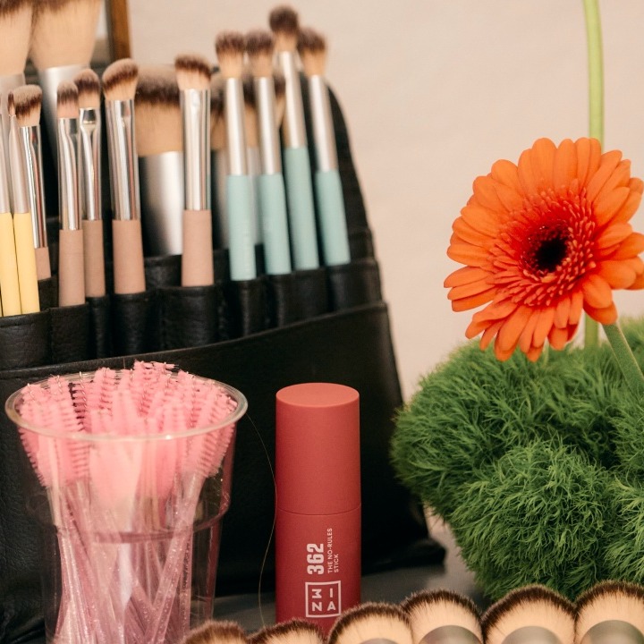 Un set de brochas de maquillaje junto a una flor naranja
