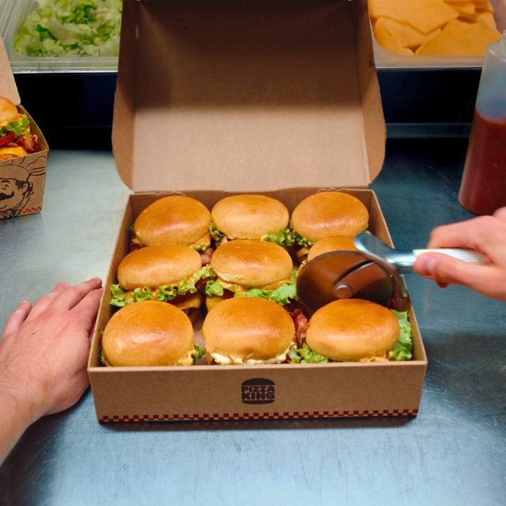9 mini hamburguesas en una caja cuadrada y una mano con el rodillo de cortar pizza