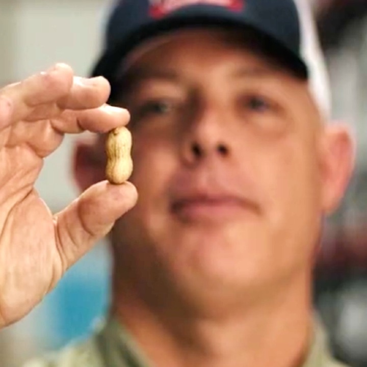 Un hombre con gorra sostiene un cacahuete con cáscara en la mano