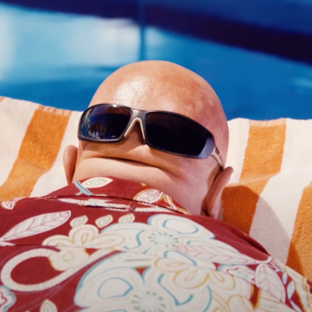 Persona calva tomando el sol en una piscina boca abajo, con unas gafas de sol sobre la nuca