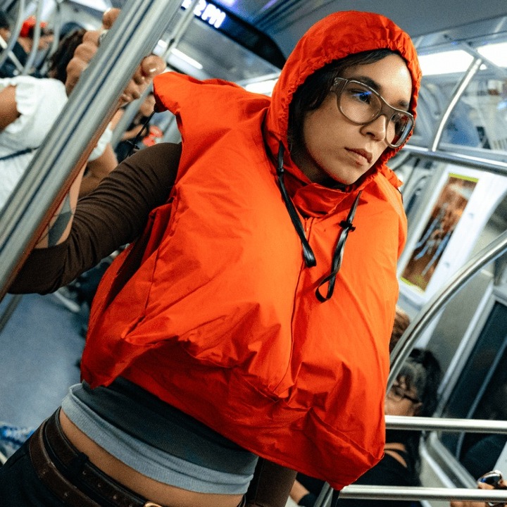 Una chica en un vagón de metro con el chaleco naranja puesto