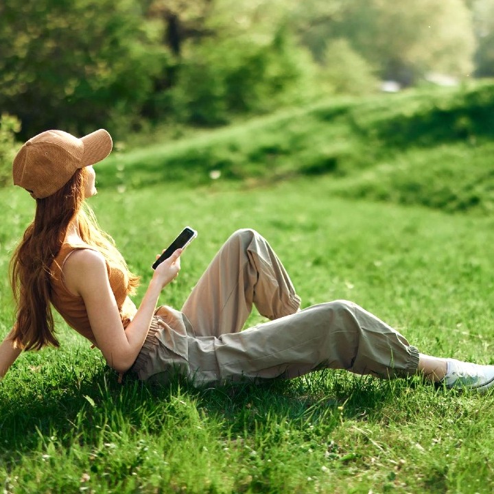Una chica con gorra sentada en el campo con un teléfono en la mano