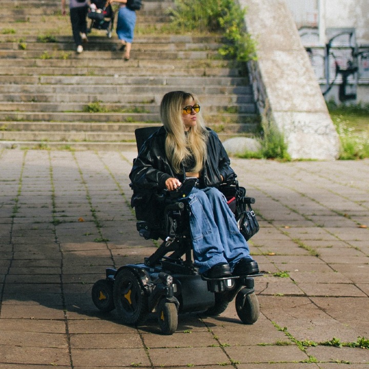 Una chica en silla de ruedas y unas escaleras detrás