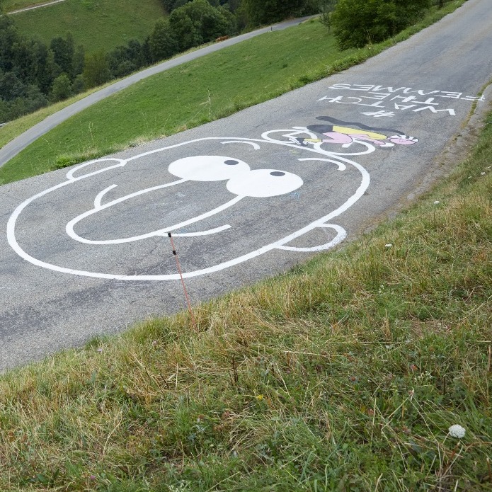un grafiti en la carretera que dice watch the femmes junto al dibujo de una cara con nariz con forma de pene