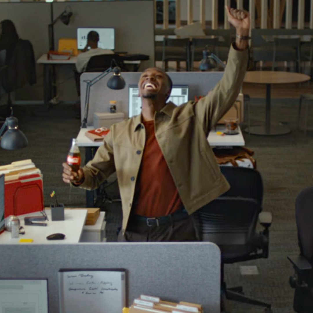 Un hombre en una oficina celebra un gol con una coca-cola en la mano