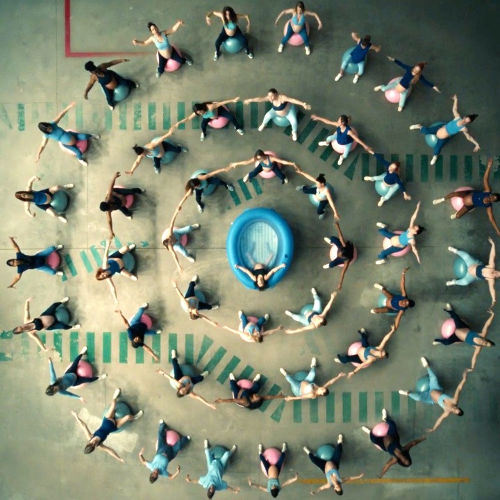 Un círculo de mujeres sobre pelotas de pilates alrededor de una piscina hinchable