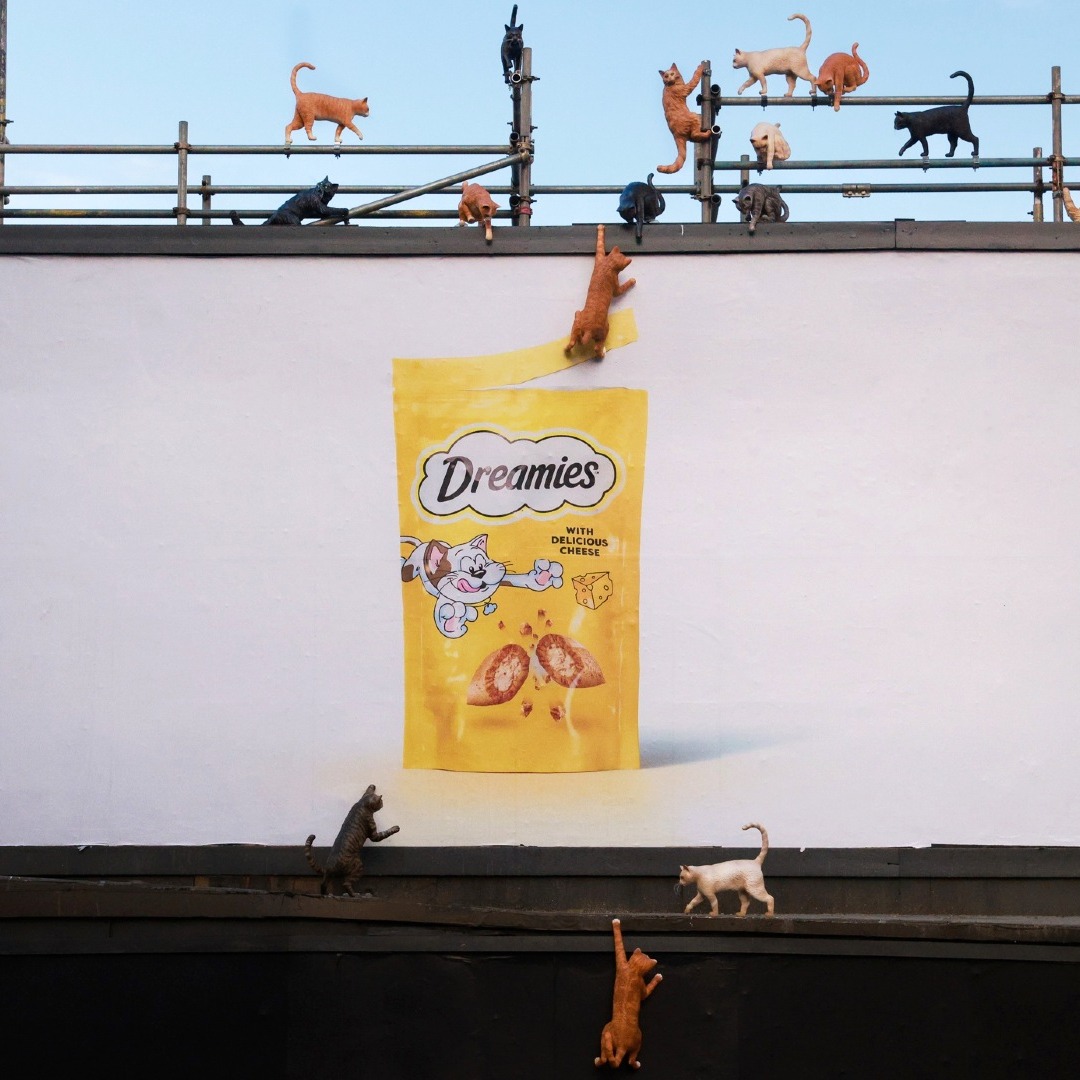Valla publicitaria de Dreamies con maquetas de gatos escalándola