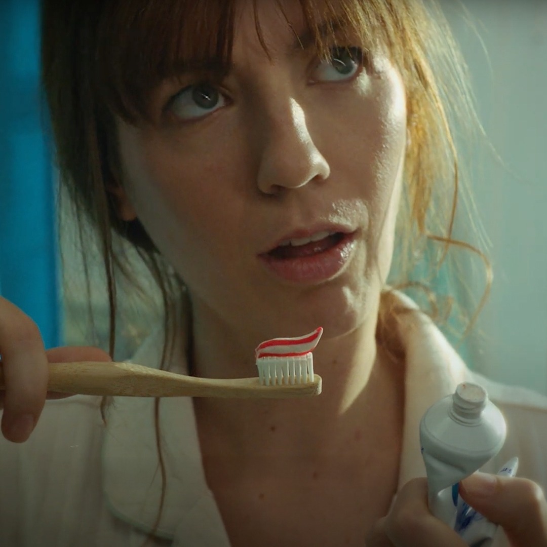 Mujer joven con un cepillo de dientes en la mano, dentro de un baño.
