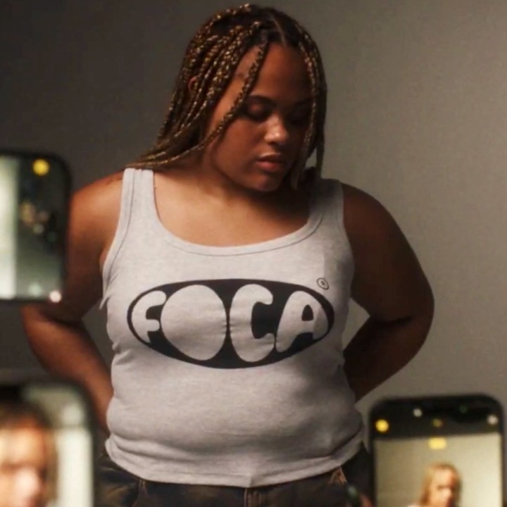 Una chica lleva una camiseta que reza "foca" muentras varias manos con móviles le hacen fotos