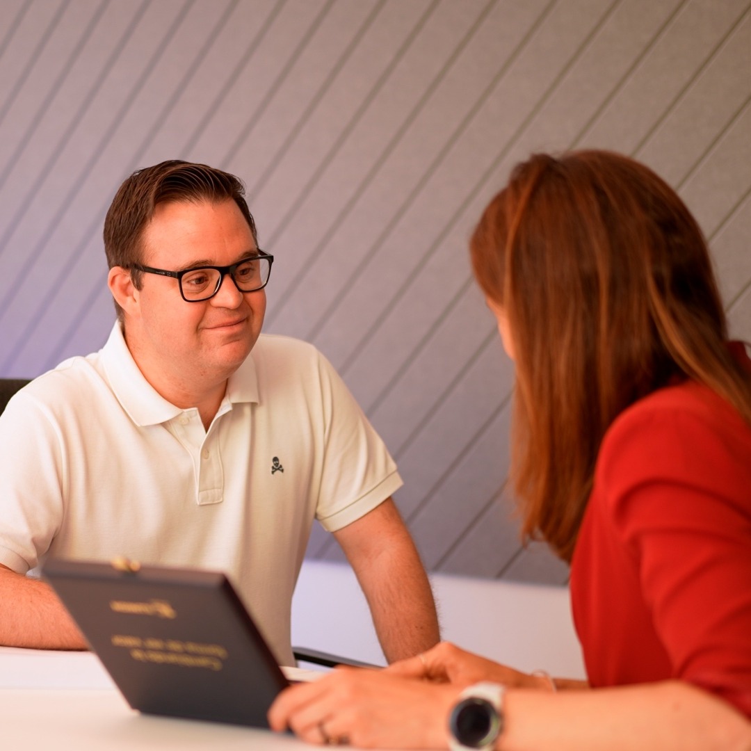 Un joven con síndrome de down habla con una mujer vestida de rojo sentado en una mesa