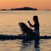 Una chica y su perro en la tabla de paddle surf al atardecer en el mar