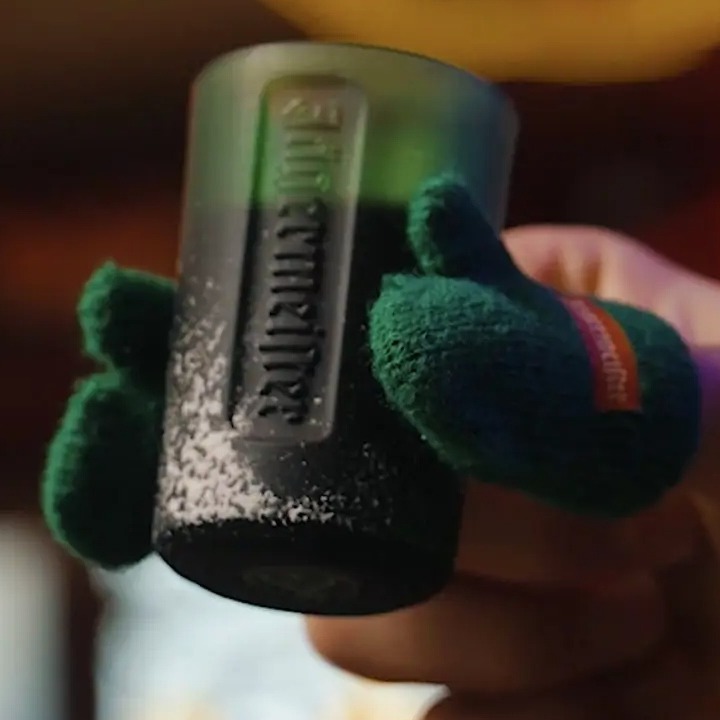 Una mano sosteniendo un chupito con guantes en el dedo pulgar e índice