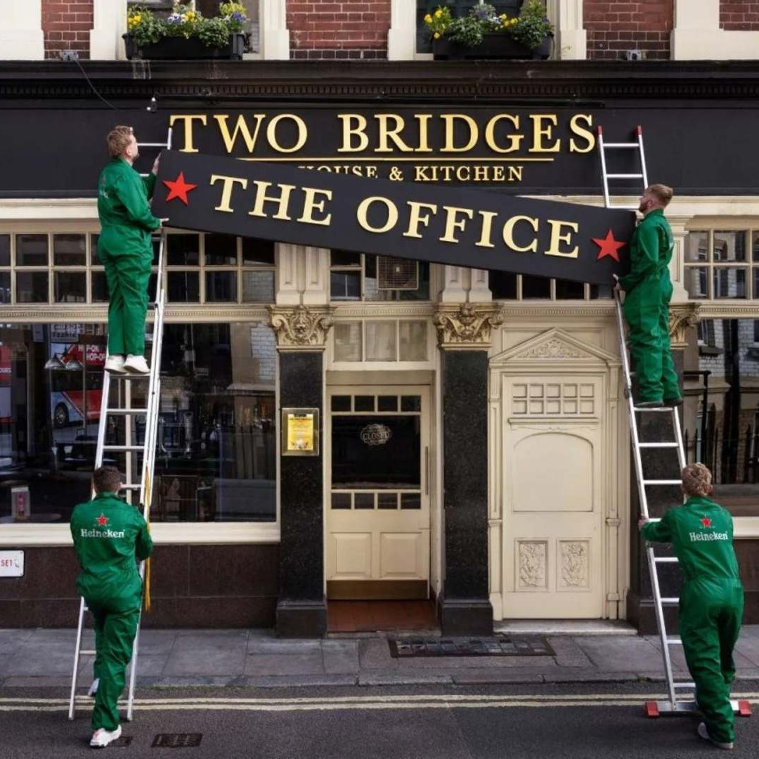 Trabajadores con monos de Heineken colocan un cartel en la fachada de un pub