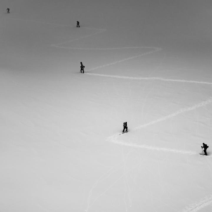 Una montaña con 5 esquiadores de fondo subiendo por el camino que ha trazo el primero