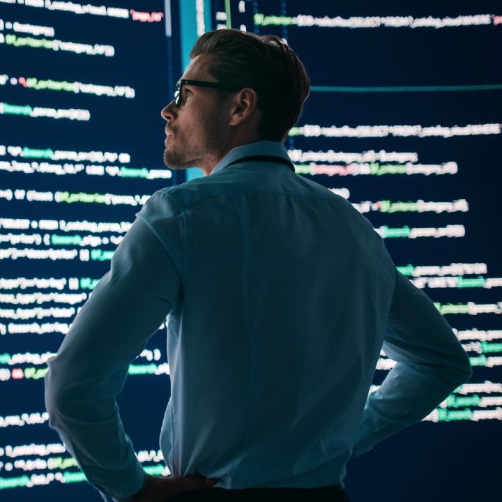 Un hombre con los brazos en jarras mira unas pantallas grandes con código HTML