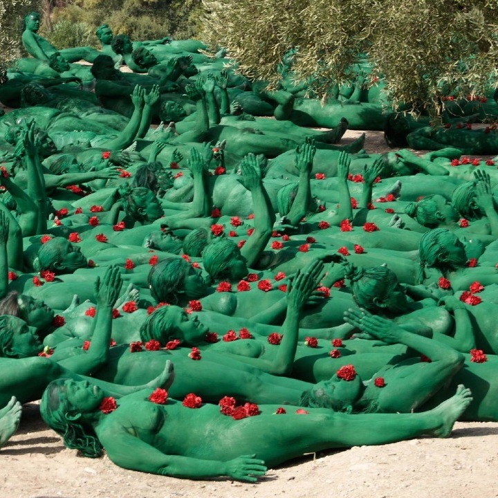 personas con el cuerpo pintado de verde tumbadas en el suelo en el campo