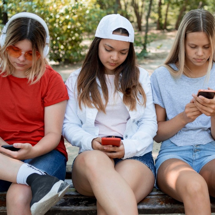 Jóvenes sentados en un banco del parque mirando el teléfono