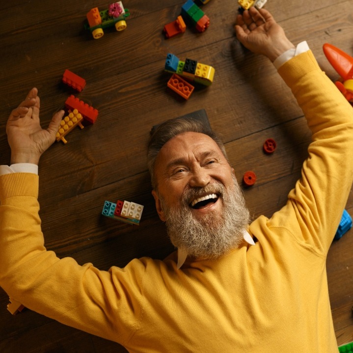 Un hombre mayor tumbado en el suelo rodeado de piezas de Lego