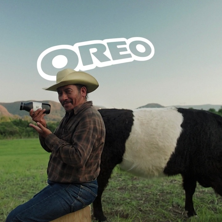 Un granjero posando con la botella de leche de vaca Oreo y detrás una vaca Belted Galloway