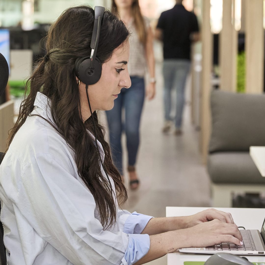 Mujer trabajando delante del ordenador con auriculares