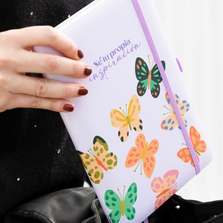 Una mano de mujer sosteniendo una libreta en la que se lee la frase "Sé tu propia inspiración"