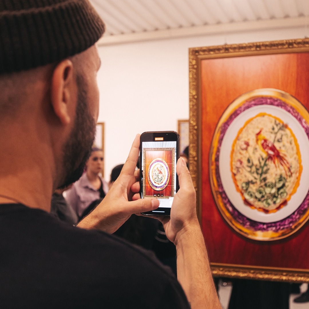Persona joven de espaldas haciendo una foto con su móvil a uno de los cuadros de ensalada de patatas, de la exposición "Food Art", integrada en la campaña "Mayonismo" de Hellmann's Brasil