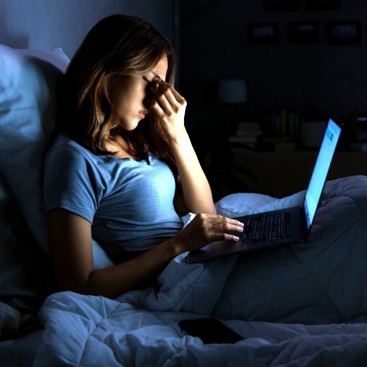 Una mujer en la cama con gesto de preocupación sosteniendo el portátil en las piernas