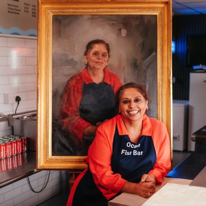 Una mujer en la cocina de su restaurante posando junto a su cuadro