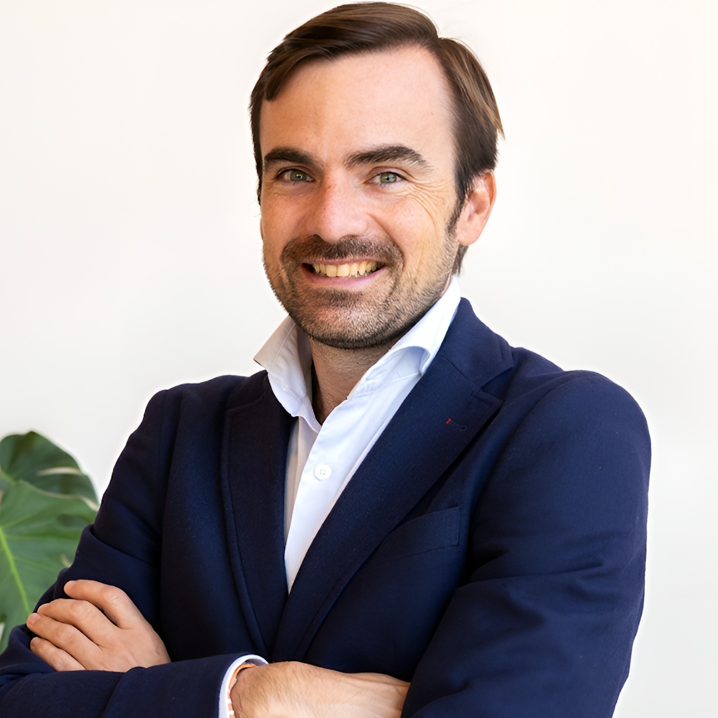 Posado corporativo de Nacho Navarro en traje y con los brazos cruzados al lado de una planta