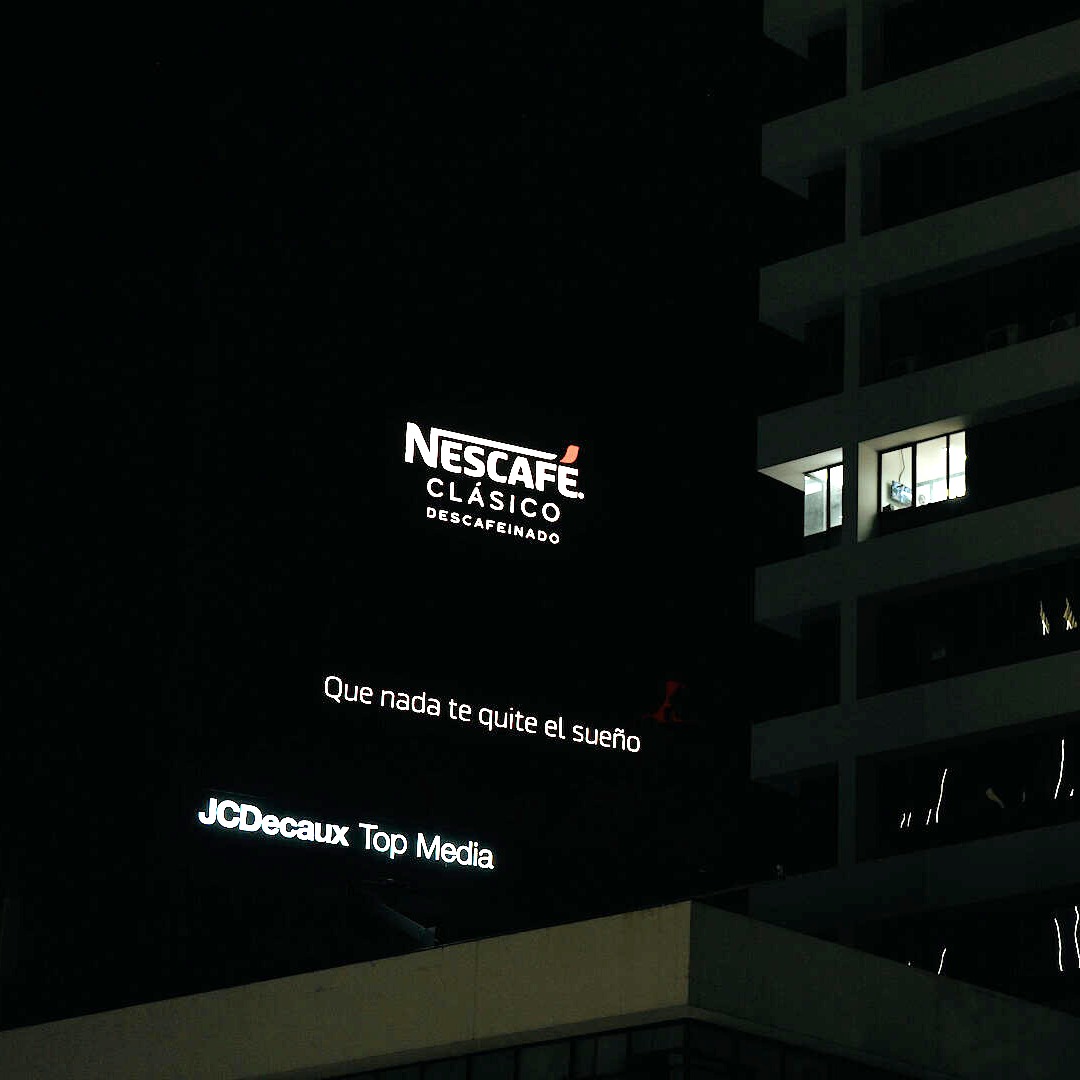 Valla publicitaria de Nescafé por la noche frente a un edificio de viviendas