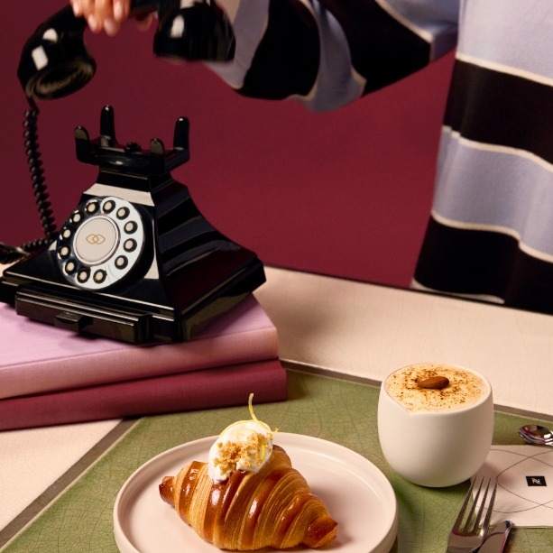 Un croissant, el café en un vaso y una cafetera de Nespresso con el cartel de molestar