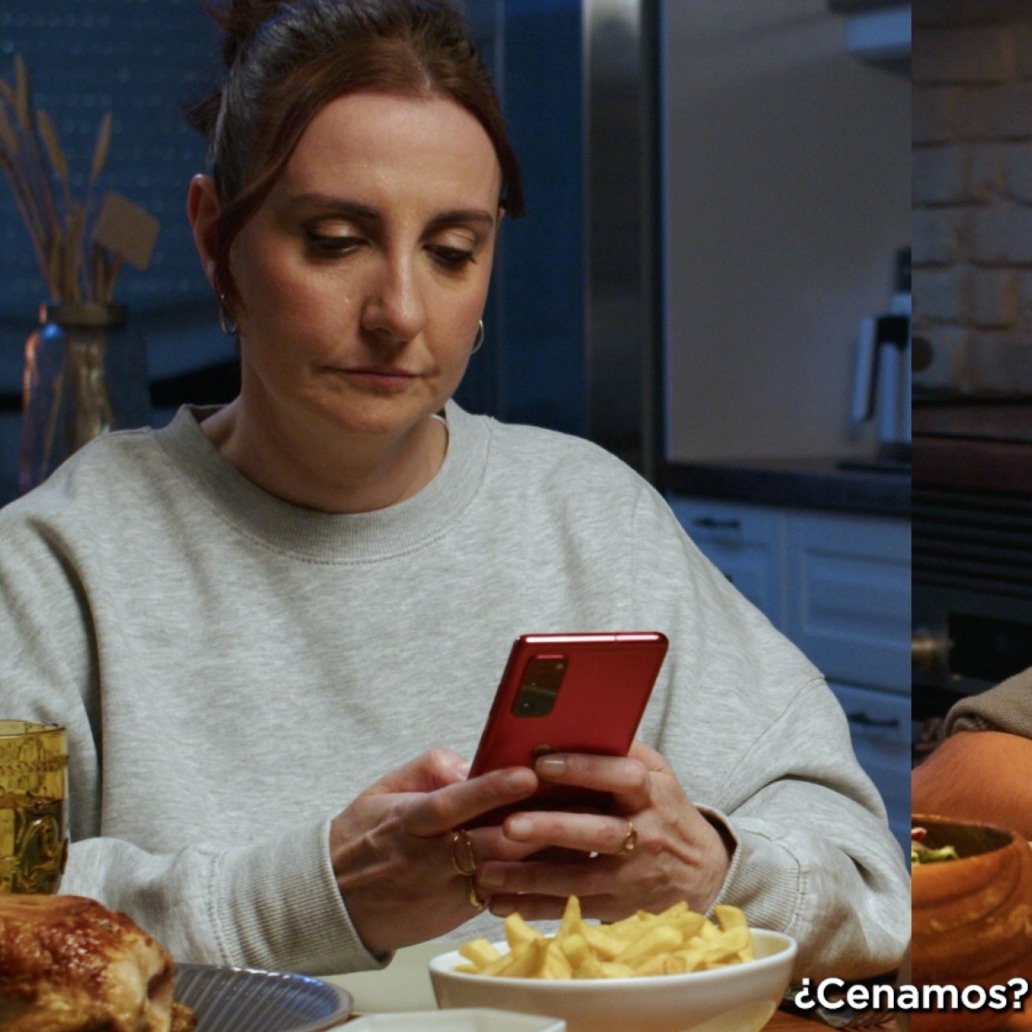 una madre usa el movil en la mesa mientras su hijo espera mirándola para empezar a cenar