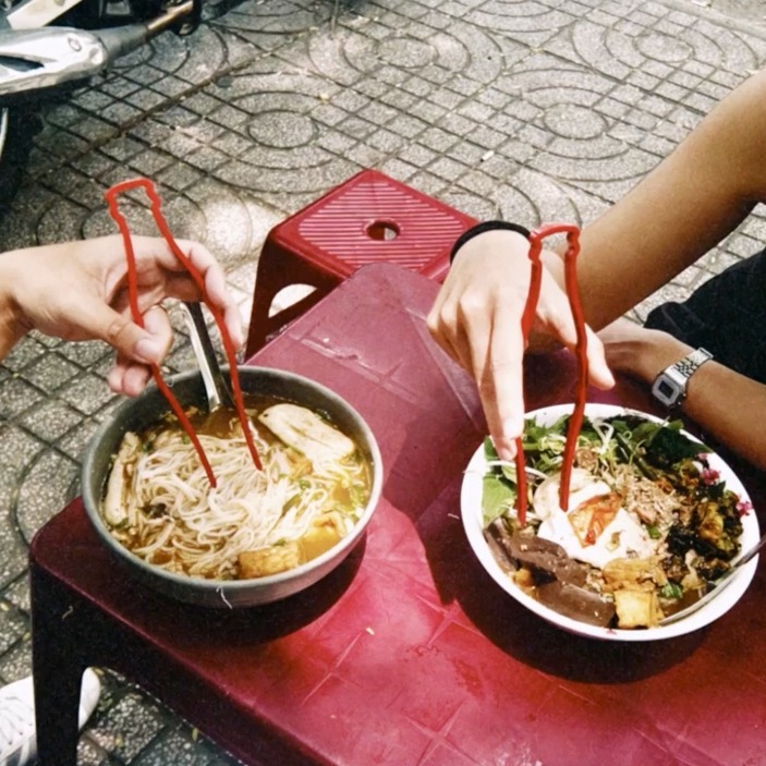 Una pareja comiendo ramen con los palillos rojos de coca-cola