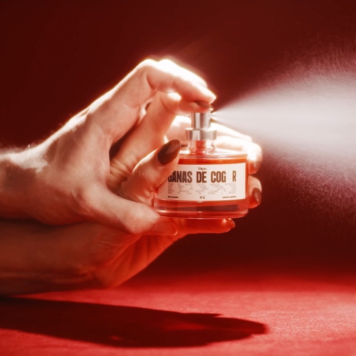 Las manos de un hombre y una mujer sosteniendo el bote del que sale perfume