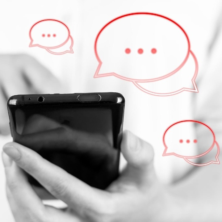 Unas manos sosteniendo un móvil en blanco y negro y bocadillos de conversación en rojo alrededor