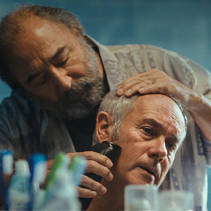 Un hombre pasando la maquinilla de afeitar a otro por la barba