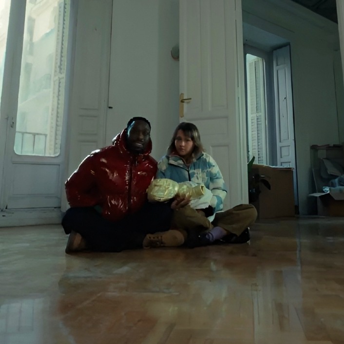 Una pareja sentada en el suelo de un salón vacío con su bebé en brazos