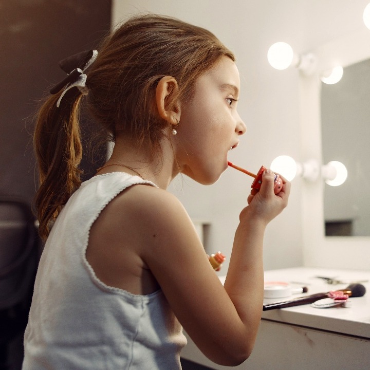 Una niña pequeña maquillándose en un espejo con un teléfono que graba